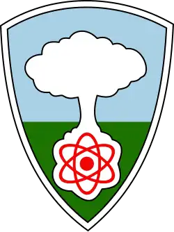 A shield with a white mushroom cloud rising from a red atom against a blue sky