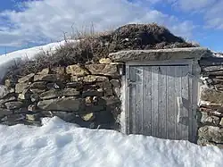 A wooden door, set into a stone frame, partially covered by snow