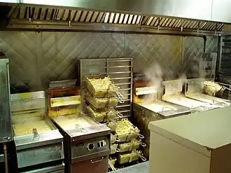 A row of five deep fryers, all steaming and filled with baskets of French fries.