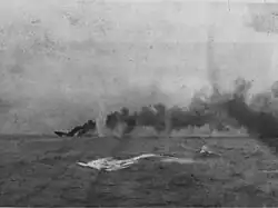 A large ship is sinking in the distance; a large dense cloud of smoke emanates from the wreck.