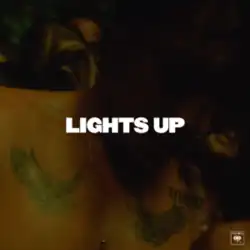 A dimly lit photo of Harry Styles showing his bare chest with two tattoos below each shoulder. The title of the song "Lights Up" is written in all caps in white at the center of the photo.