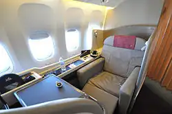 A light mocha colored seat with ottoman, table, and enclosure and four unshaded windows on the left