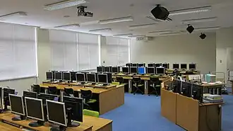 A side view of a language laboratory. There are four rows of computers and a control desk at the front of the room.