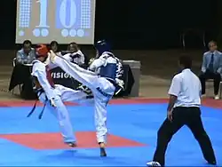 Two martial artists in gis on a mat, with one kicking the other in the head