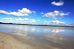 The photo shows Lake Beeac and the sky above it. The surface of the water is mirror-like, it reflects the blue sky and the clouds in it.