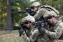 US Army 10th Mountain Division soldiers; (bottom‑left) AN/PEQ-15 attached to an M4 carbine; (bottom‑right) DBAL-A2 attached to M249 SAW.