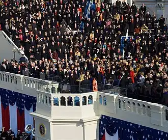 View of a large portion of a large ceremony with visible red, white and blue ornamentation and a crowd of attendees