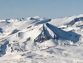 A snow-covered, pyramid-shaped mountain peak in a snow-covered, mountainous landscape