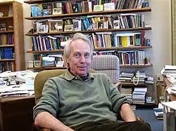 Colour photograph of Antony Jameson in pullover, relaxed, seated in a study with many books and papers