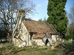 A simple chapel with a bellcote and a protruding porch, and winter trees behind