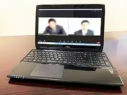 A laptop is sitting on a desk. The screen is divided in half showing blurred images of two people video conferencing.