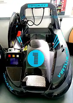 The sit-down version of the Virtuality arcade unit. The unit is a seat with two fixed position joysticks either side for game control. The headset is mounted on a hook.