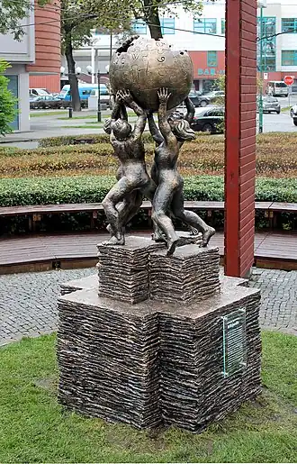 A monument depicting a group of 4 people holding up an incomplete sphere made of jigsaw puzzle pieces.